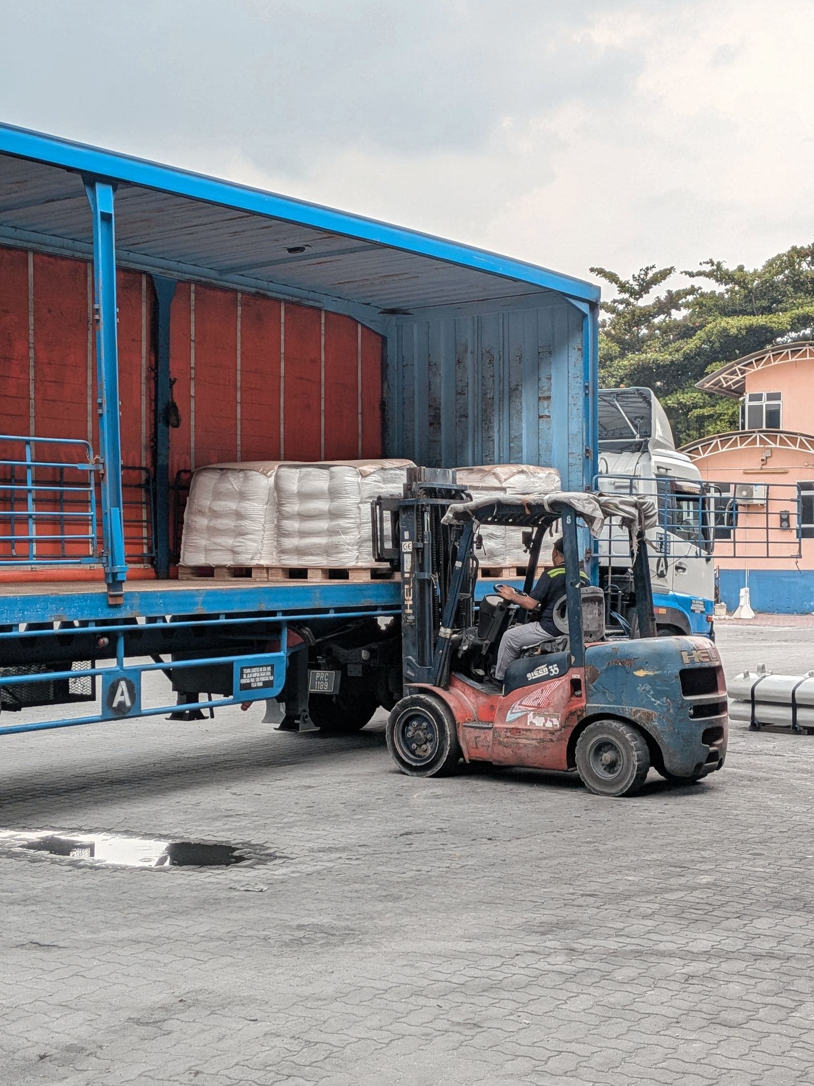 Forklift loading palletized freight onto a flatbed trailer at a distribution warehouse